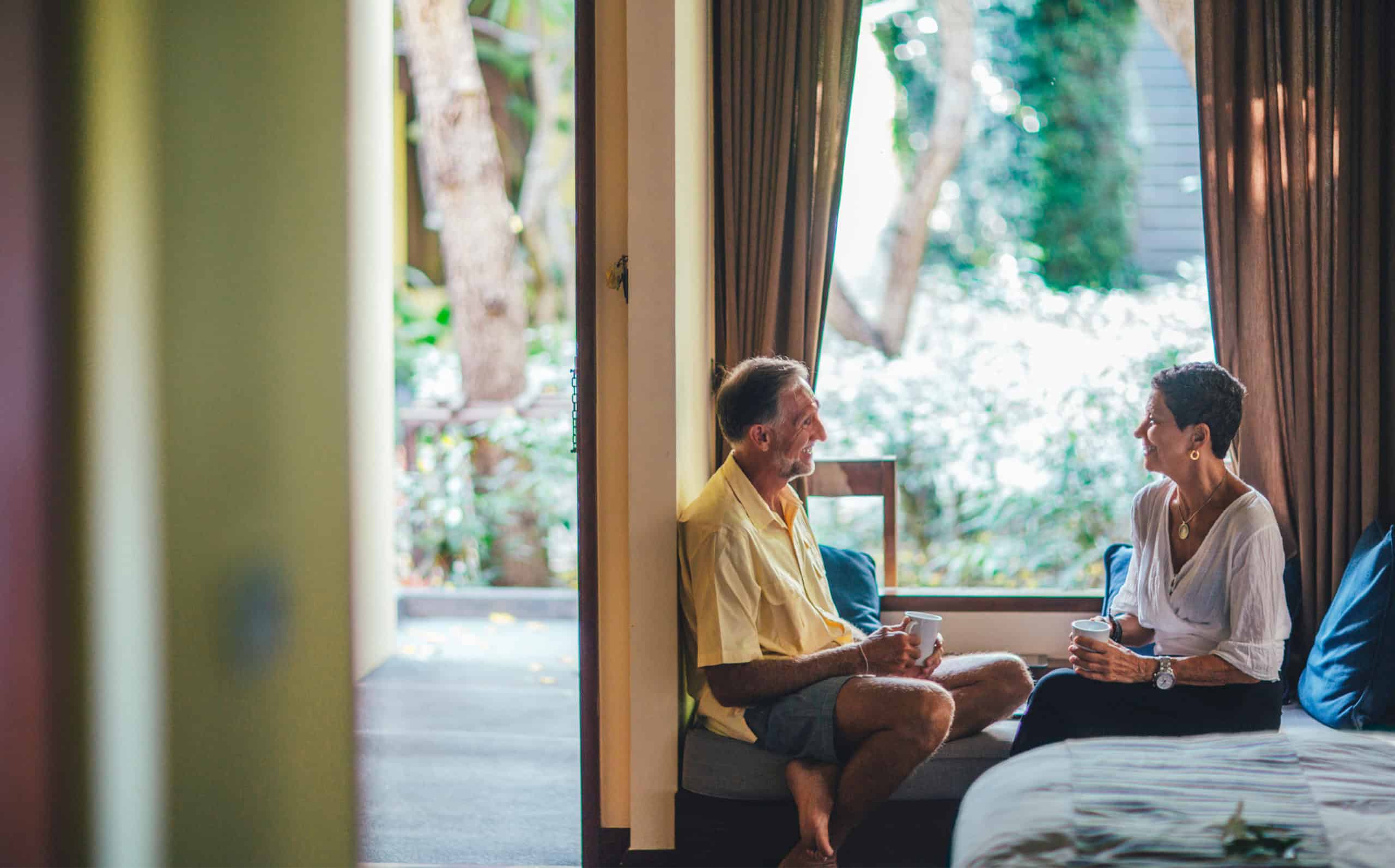 Mature couple sitting by a window, talking about their communication retirement plan.