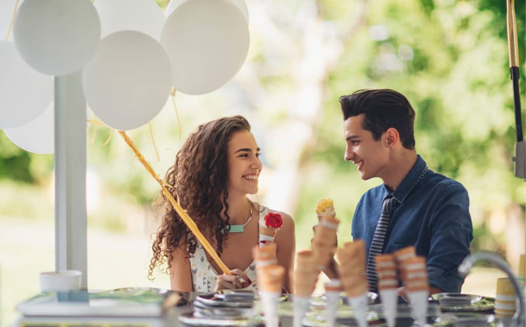 A young couple smiles at each other while they eat ice cream