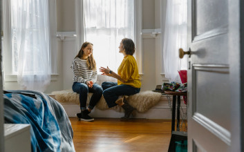 A mother and daughter sit on a window bench while having a serious conversation, setting boundaries, and bonding.