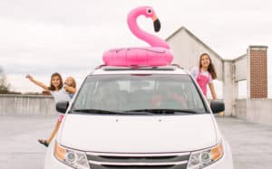 A photo of a family in a parked car. The children are excited and leaning out of the car.