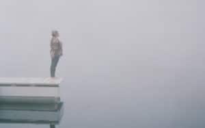 A woman standing at the end of a pier in fog.