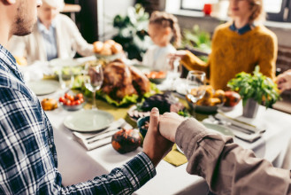 Family praying together as they sit around the dining table for a holiday meal