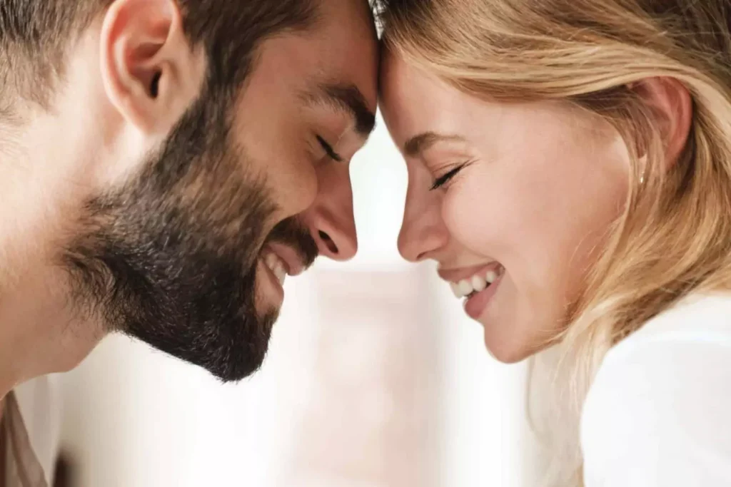 A joyful couple leans their foreheads together with eyes closed and smiles on their faces, symbolizing spiritual unity in marriage.