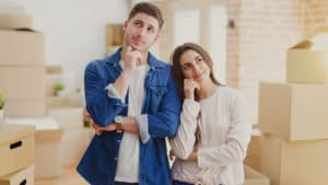 Couple standing in front of a recently moved-in house wondering if they should start a family