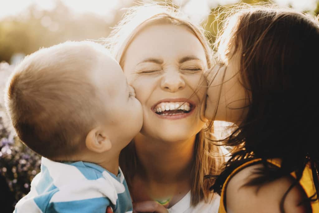 Close up of laughing mom being kissed on each cheek by her young son and daughter