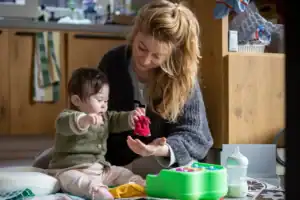 Mother sitting on the floor playing with her baby, encouraging learning and bonding through simple play.