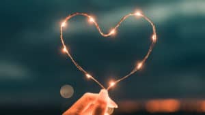 Close up of a heart-shaped string of lights held up by a woman's hand