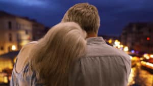 A man and a woman gaze over a canal and city lights