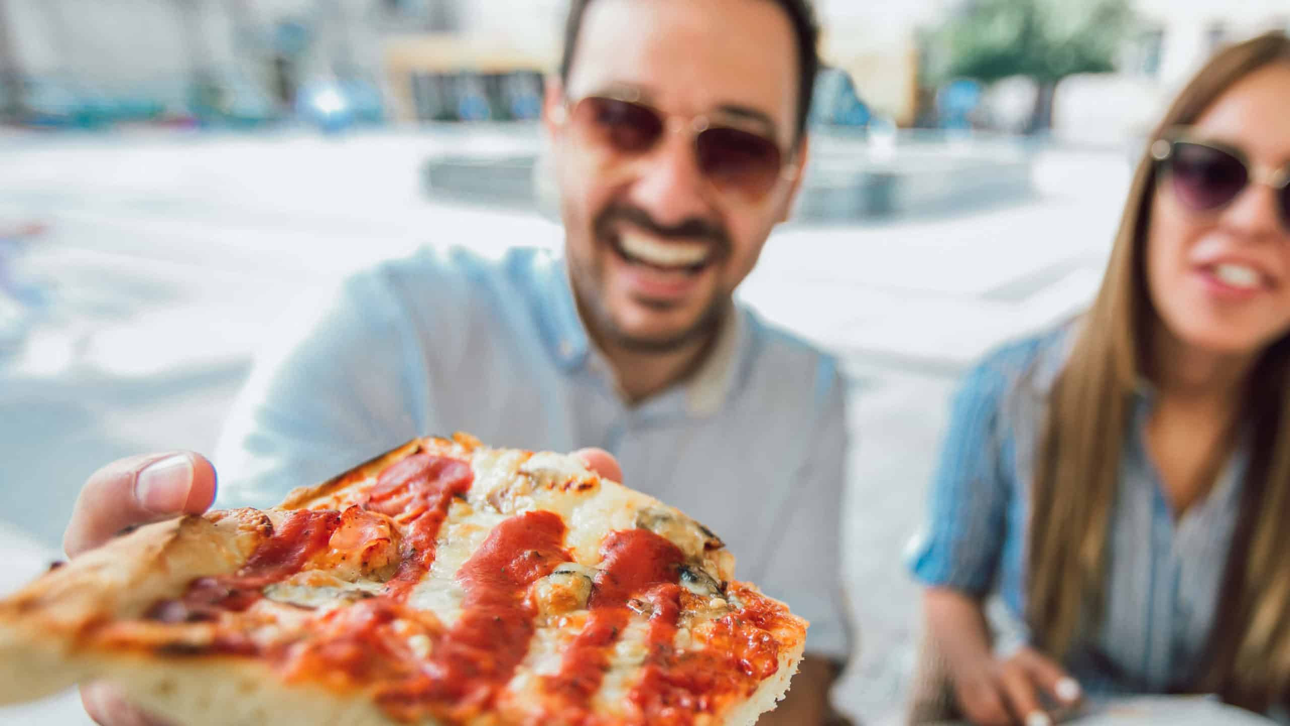 a man offers a gust a slice of pizza