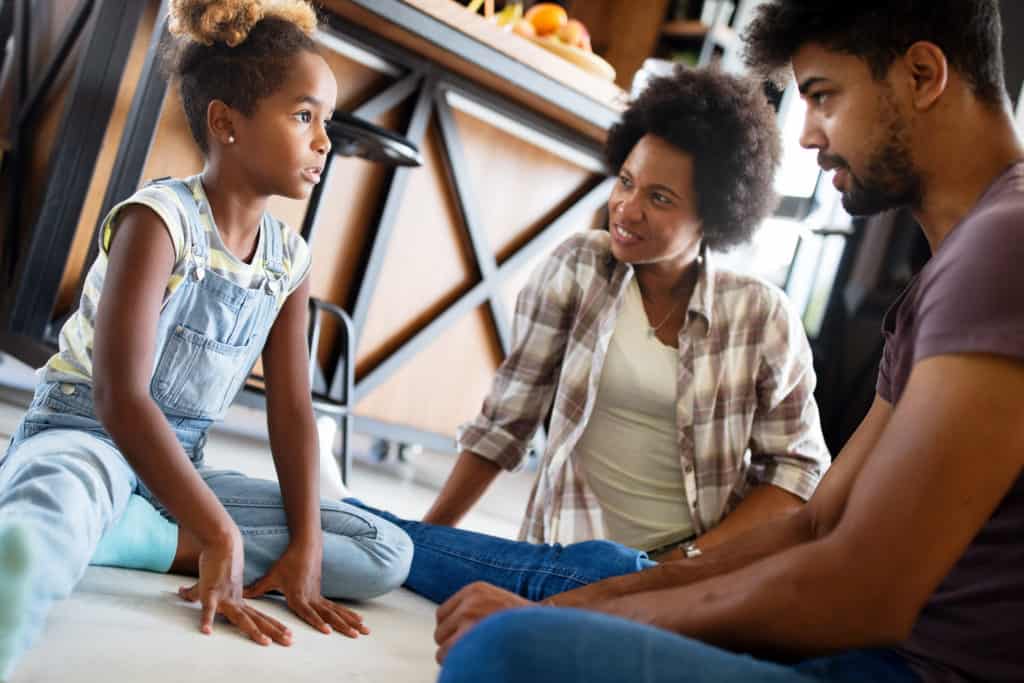 Couple and their young daughter talking with each other while sitting on the floor in their home