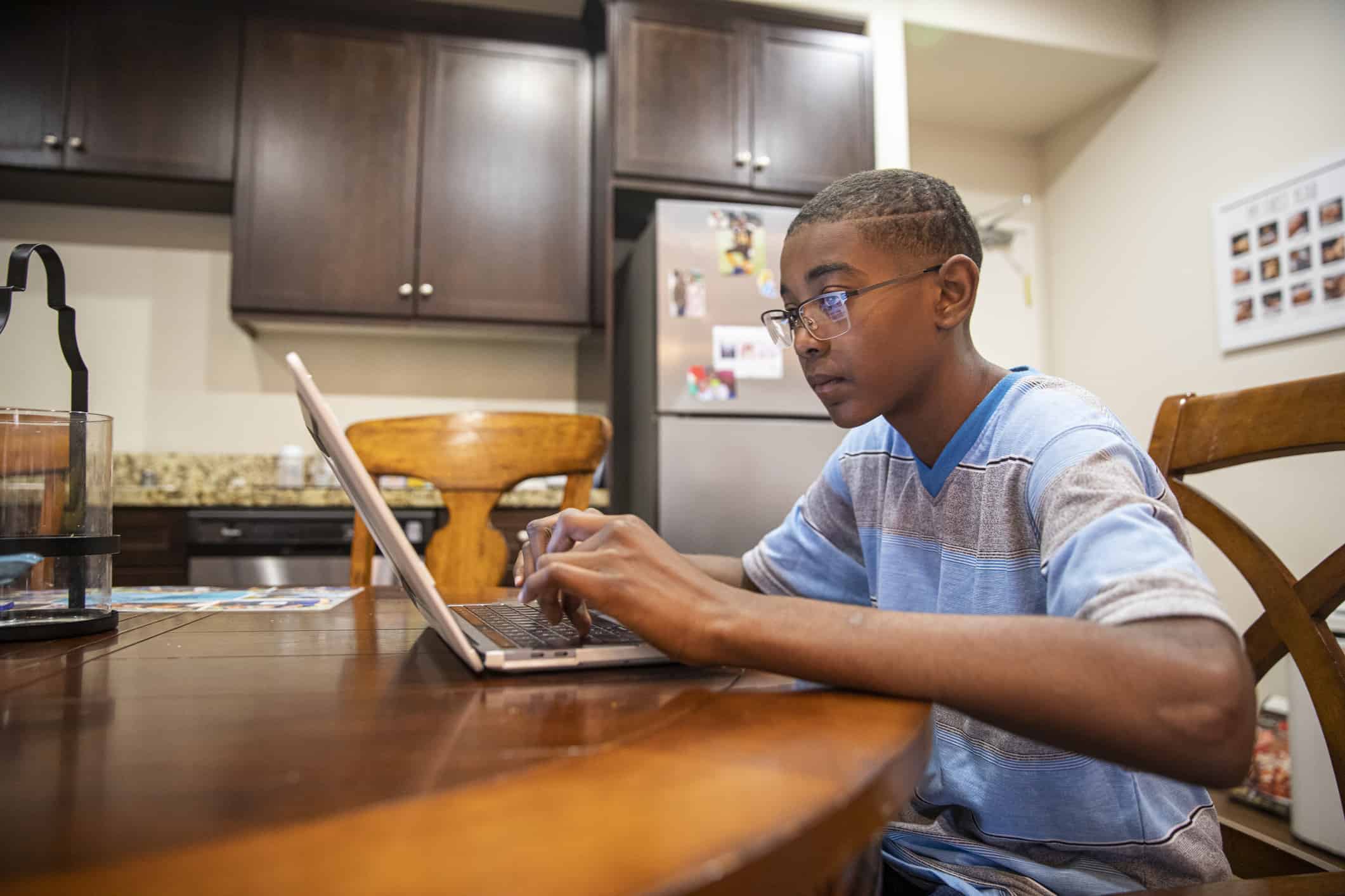African American tween boy typing on a laptop at the kitchen table