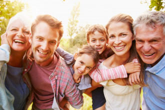 Happy family of parents, two young children, and grandparents posing for the camera outside