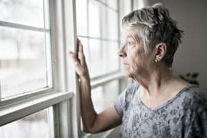 An elderly woman looks out her window.