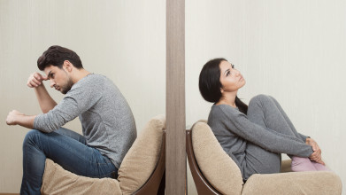 Couple separated by a wall, sitting and facing in opposite directions, suggesting a troubled relationship