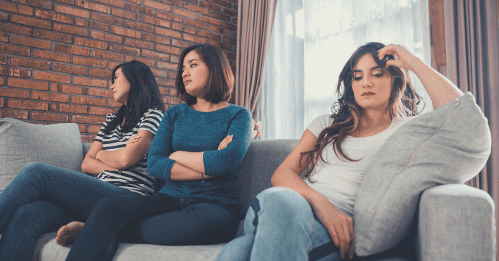 Three upset young women sitting on a couch, avoiding looking at each other.
