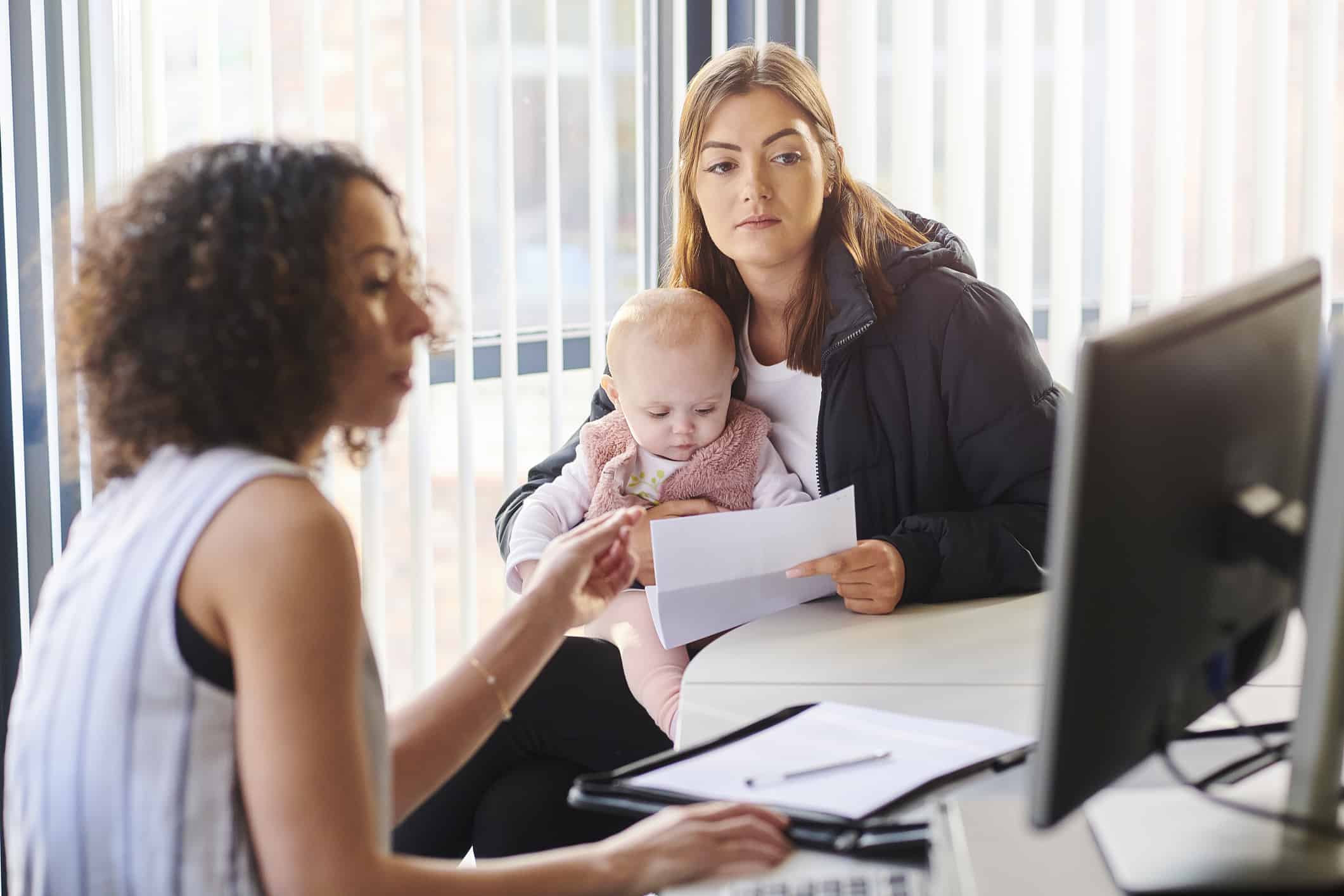 Young mom with her baby in her lap being shown something on a computer screen by a professional woman