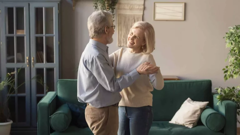 A joyful older couple dances together in their cozy living room, embracing the empty nest phase with love and companionship.