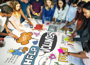 Group of young adults gathered around and working on a large sign promoting volunteering