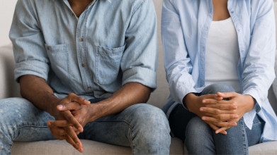 A man and woman sit together with hands crossed.
