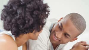 A Black couple talks while laying across a bed