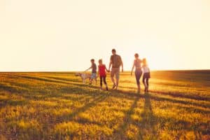 Shown from behind, a family of five walking with their dog through a field at sunset