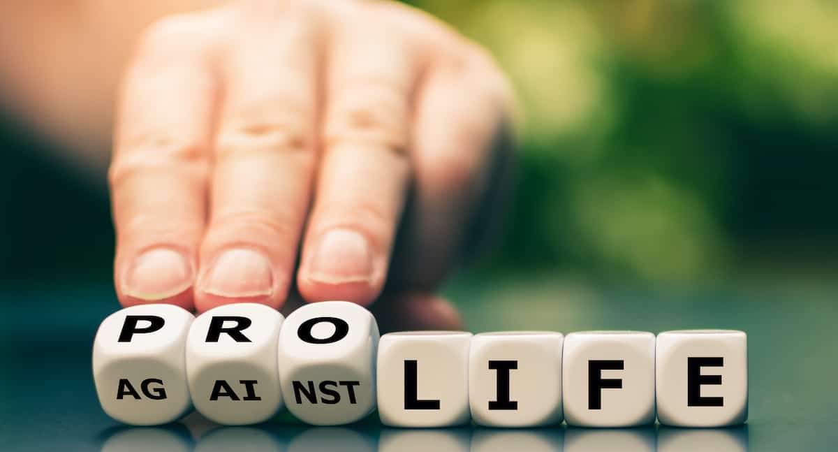 hands turning dice that say pro-life or against life.