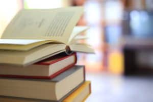 Stack of books on a table with a bookshelf in the background