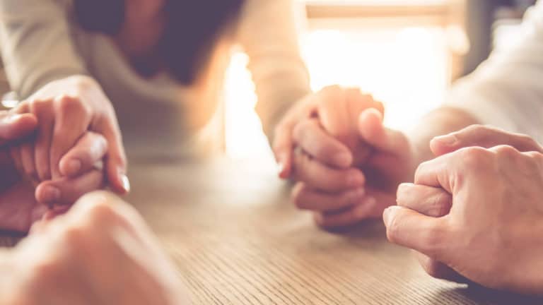 A group of men and women hold hands and pray