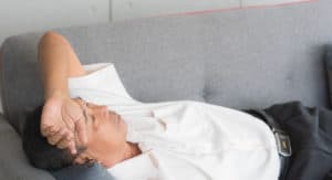 Senior Asian man sleeping on couch feeling sick and migraine from tired and health problems