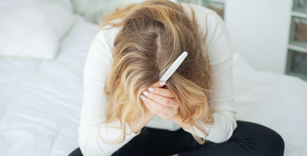 A young woman holding her head in her hands, distraught over the results of a pregnancy test