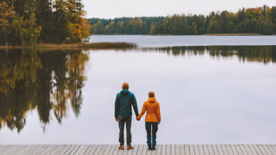 Couple holding hands looking out at autumn trees surrounding lake