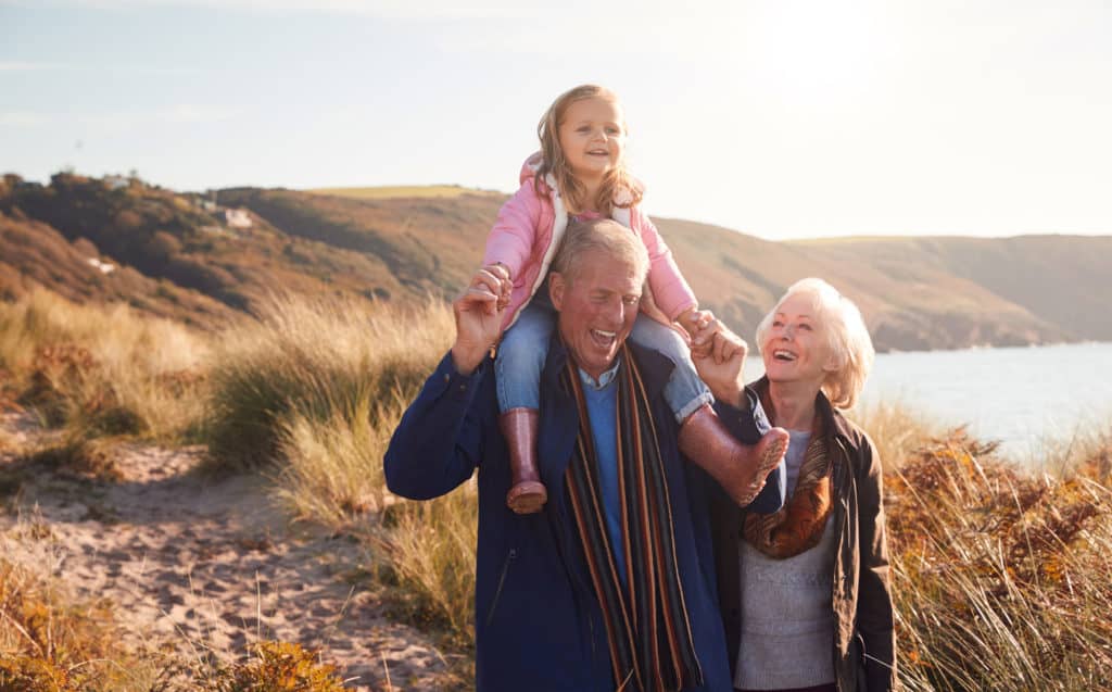 things to do with grandkids - Grandfather Giving Granddaughter Ride On Shoulders As They Walk Through Sand Dunes With Grandmother