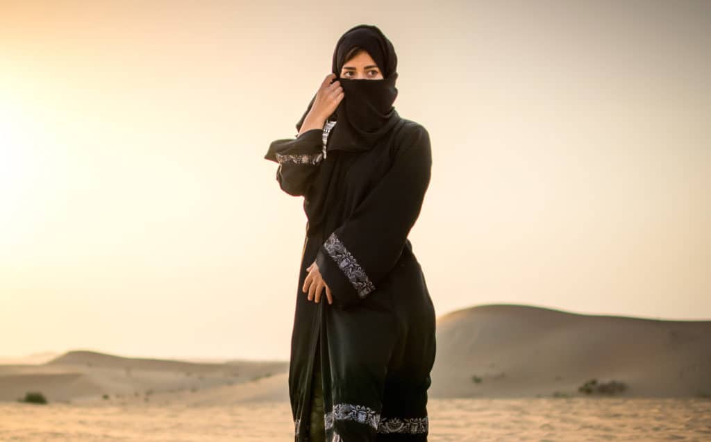 muslim - Full length portrait of Arab woman in burka clothing standing in the desert.