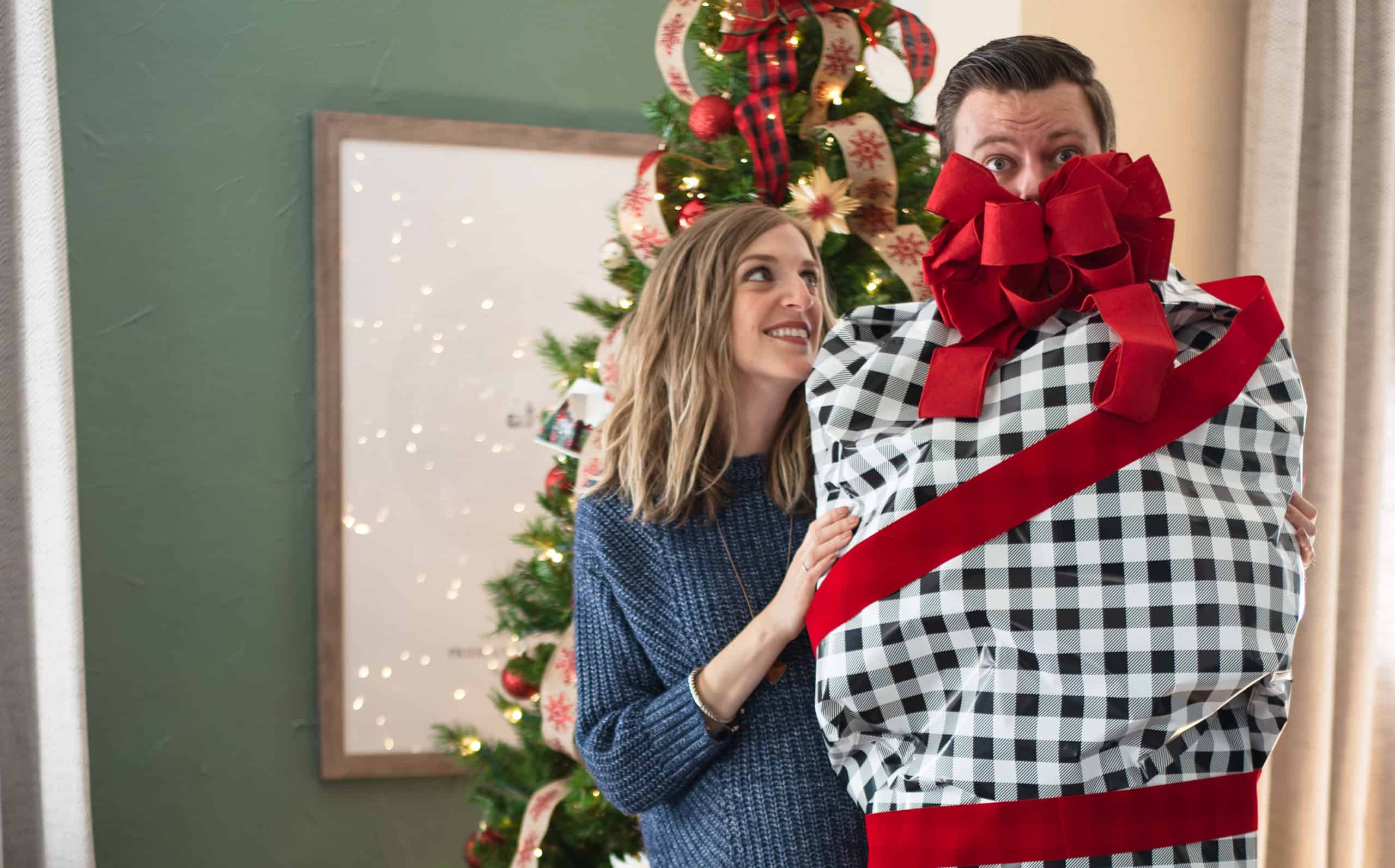 what does your spouse really want for Christmas - Wife looking at husband who is wrapped up in Christmas wrapping paper