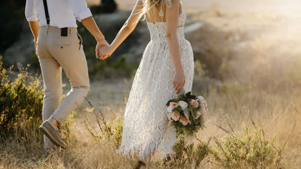 A newlywed couple walks through a field holding hands, confident in what they learned from the words of wisdom given to them that their marriage will succeed.