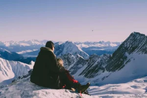 A couple sitting on a snowy mountain peak, gazing at the distant snow-covered mountains. Their body language suggests deep contemplation, possibly reflecting on overcoming marriage problems as they navigate their relationship challenges in a serene yet isolating landscape.