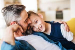 Mature father with small son sitting on sofa indoors, resting.