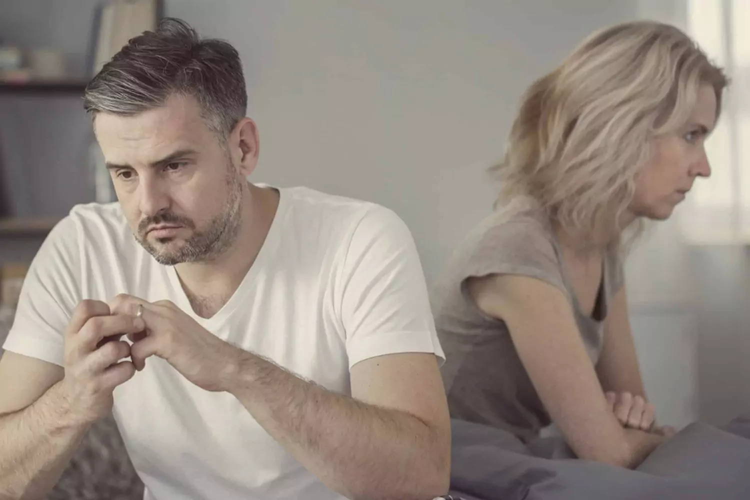 Depressed middle-age couple seated in different directions. He’s toying with his wedding band, implying a troubled marriage and the need for a healing separation.