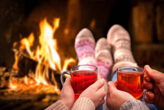 Couple enjoying cups of tea as they snuggle together while wearing cozy socks and sitting in front of the fireplace