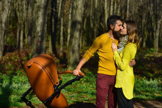 Couple pausing for a romantic brace while pushing their baby stroller in a walk through a forest