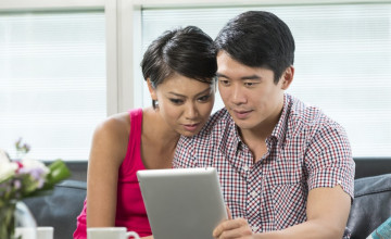 Asian couple sitting on a couch reading a tablet together