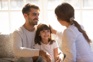 Mom and dad sitting with their young smiling daughter, mom stroking the side of her head