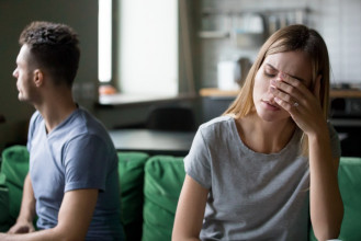 Upset married couple sitting, facing away from each other on a couch