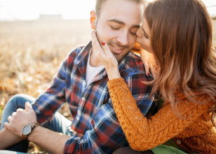 Wife kissing husband's cheek, her hand resting on his other cheek as they sit outside