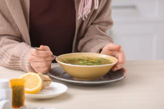 Close up of a bowl of soup and a woman's hands around it, one hand holding a spoon