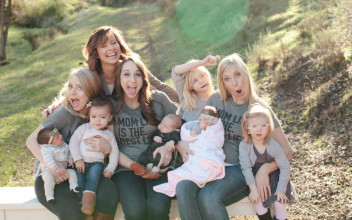 Group of moms smiling, laughing and acting silly for the camera as they sit outside with their young children