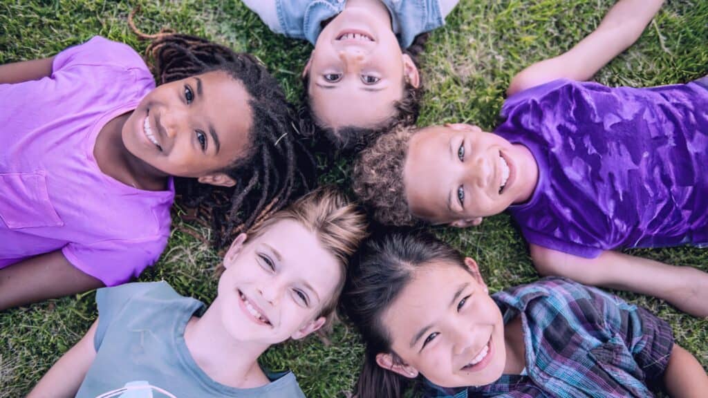 Cover image for "10 Ways to Make a Difference for Children in Foster Care" in which a circle of children are laying down in grass and smiling looking up at the camera.
