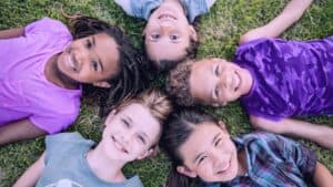 Cover image for "10 Ways to Make a Difference for Children in Foster Care" in which a circle of children are laying down in grass and smiling looking up at the camera.