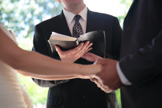 Photo of a pastor conducting a wedding with the married couple holding hands.