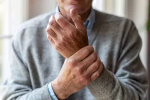 An elderly man wearing a gray sweater clutches his wrist in discomfort, illustrating the impact of chronic pain on daily life and relationships, including marriage. The image conveys the physical and emotional burden that ongoing pain can place on individuals and their spouses.